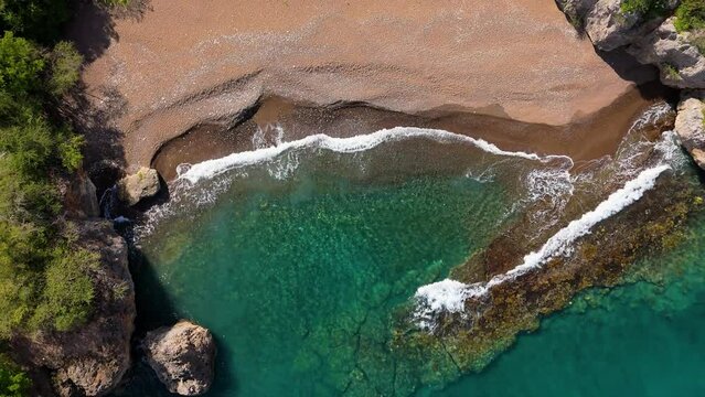Drone rises above playa Santu Pretu black sand beach with ocean waves crashing on sheet rock