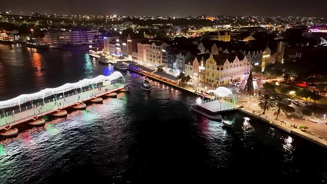 Tug boat exits around Queen Emma pontoon bridge lit up at night, aerial
