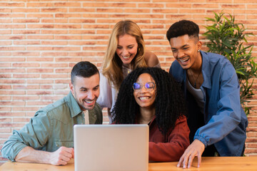 Group of young adult friends in front of the laptop in a apartment. Multiracial group using a computer and doing a brainstorming and working together, smiling and planning and idea