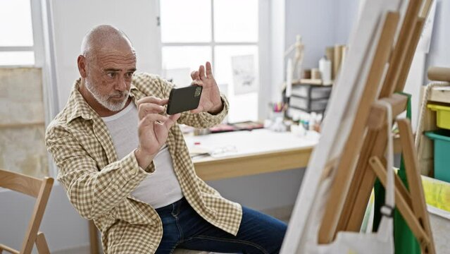 Mature man with grey beard texting on smartphone in art studio setting