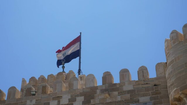 An Egyptian flag flys in the wind over the Citadel of Qaitbay with the blue sky in the background. It is very windy over this fort.