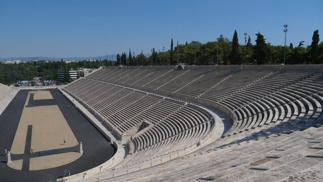 Panning shot of greek amphitheater in Athens where the olympics were first held. It is a bright sunny day and we can see the entire field over the marble bleachers where many historic games happened.