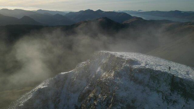 Hiker reaching summit of snowy mountain with clouds swirling Stob Ban Highlands Scotland