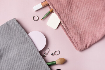 A Gray and Pink makeup cosmetic bag with cosmetic beauty tools and product spilling out on to a pastel colored pink background Top View Earrings