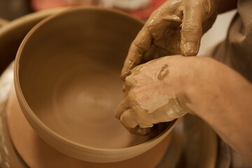 Ceramist shaping a bowl with his hands on a wheel in a studio