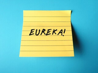 Yellow note stick on blue background with handwritten text EUREKA! means 