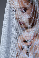 Portrait of a young woman covered with white mesh fabric. A woman hides her face behind a veil cloth.