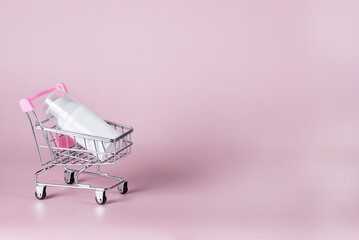 White cosmetic jar with cream lie in a shopping trolley on a pink background Online home shopping Sale or shopping Background