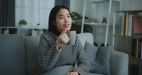 Portrait of Relaxing young woman holding cup enjoy smell coffee or tea and drinking with happiness in morning while sit on sofa in living room,Free time,take break in home,smiling
