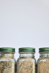 Packaging and storage of homemade seasoning. Three glass jars with green lid on gray background. Using reusable, recyclable. Aromatic Spices made from dried garlic, herbs, salt for cooking. Copy space