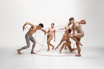Graceful ballet dancers performing with red string connected to young man against white studio...