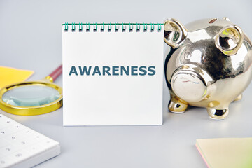 AWARENESS word writing on a notebook on a gray background near a calculator, a piggy bank, and stickers. Small Business Concept