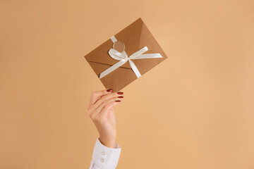 female hand hold discount card or gift certificate in envelope on studio beige background