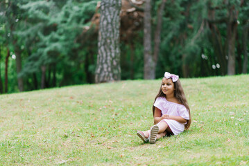 A little child girl walks in the park in the summer, sits on the grass in a clearing. summer holidays in nature