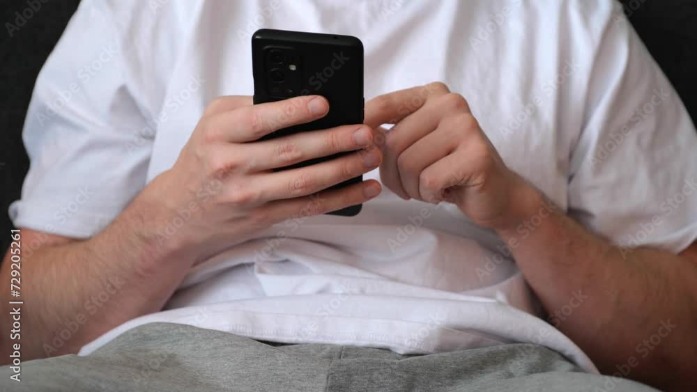 Aufkleber man scrolling his smartphone while sitting on sofa. cropped frame to focus on hands and smartphone.