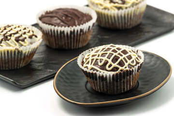 Chocolate muffins served on a black plate. Homemade dark and white chocolate cakes. White table background.
