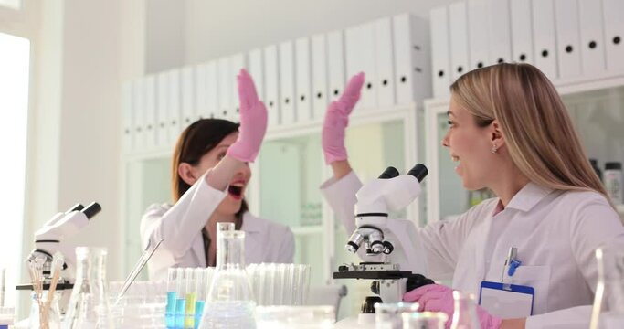 Modern medical research laboratory of young scientists using microscope and high fiving after obtaining results