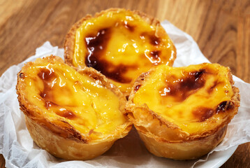 Pastel de nata tarts or Portuguese egg tart on a wooden brown background. Pastel de Belem is a small pie with a crispy puff pastry crust and a custard cream filling. Sweet dessert. - obrazy, fototapety, plakaty
