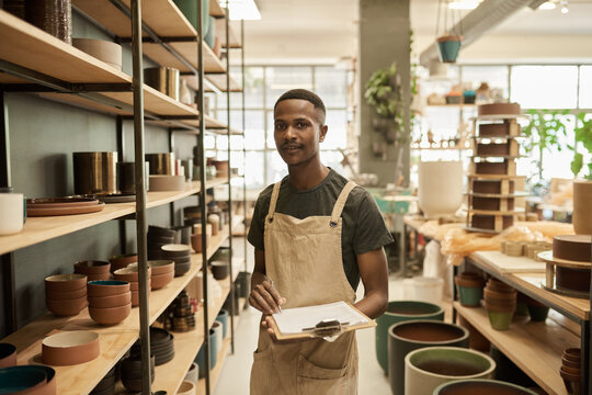 Smiling African potter doing inventory of pots on shelves in a ceramics studio
