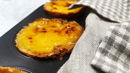 Lots of freshly baked Pastel de nata or Portuguese egg tart desserts in a baking dish. Pastel de Belme is a small pie with a crispy puff pastry crust and a custard filling. Small cupcake.