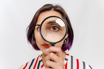 Magnifying glass. Woman's face through magnifying glass. Short hair, big eyes. Concept research.
