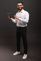 A cheerful Indian businessman in a white shirt interacts with a digital tablet, his full-body stance and engaging smile conveying accessibility and tech-savviness