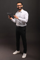 A cheerful Indian businessman in a white shirt interacts with a digital tablet, his full-body...