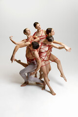 Fototapeta na wymiar Talented artistic young people, man and women, ballet dancers performing, tied with red string, dancing against white studio background. Concept of classical dance, modern style, inspiration
