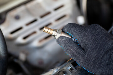 Oxygen sensor for gasoline and diesel engines in the hand against car engine. Mechanic holds oxygen sensor. lambda probe - obrazy, fototapety, plakaty
