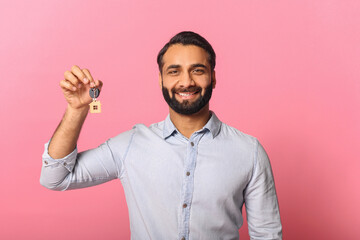 Against a vibrant pink background, an Indian businessman beams while holding up a house key,...