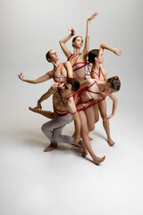 Group of ballet dancers, tied together with red strings, creating intricate pose against white studio background. Balance and harmony. Concept of classical dance, modern style, inspiration
