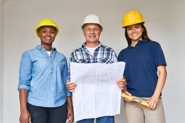 Portrait of smiling female construction workers and senior male contractor standing with blueprint...