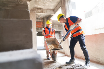 Young male and female masons working together while mixing cement at incomplete housing development