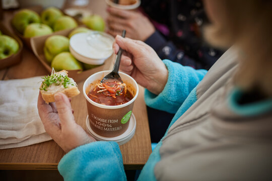 A woman eats soup from a cup made of renewable paper.