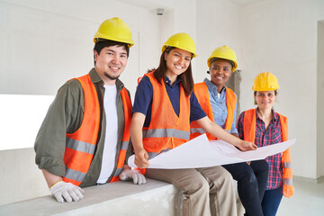 Portrait of smiling construction coworkers analyzing blueprint of house at incomplete site