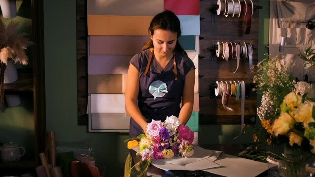 Young woman working in her flower shop making bouquet with various types of flowers.