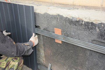 Close up on builder hands installing metal sheets to waterproof and renovate old house foundation...