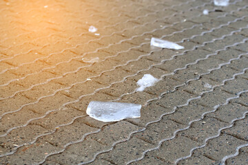 Piece of ice lies on wet paving slabs,  ice on sidewalk melting in sunny day.