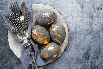 able setting. A fashionable concrete plate with a rabbit on a napkin, Easter eggs with gilding, feathers on a gray background. The concept of a Happy Easter holiday for cafes and restaurants.
