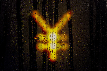 Blurred glowing Japanese yen sign made from light bulbs.The symbol of the national currency behind a rain-wet window with water drops in the night.Sign of economic crisis and business problems