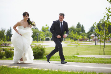 The bride and groom run along the road together
