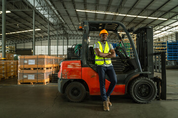 African forklift driver focused on carefully transporting stock from shelves of a large warehouse wearing a helmet and vest looking toward goods