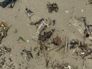 Dirty sand beach with waste and brown glass bottle trash, flat lay or top view