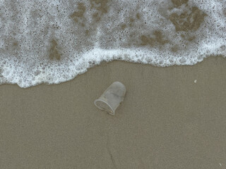 Sand beach, a plastic cup waste, and sea foam, flat lay or top view