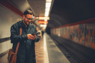 A smiling adult employee sending text messages on his phone while waiting for the train