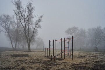 Fototapeta na wymiar A small sports ground is installed in the park, bars, gymnastic rings and rope, the most necessary for physical exercises, late autumn, morning fog