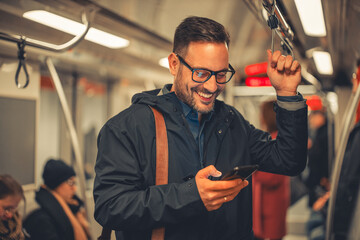 A cheerful adult businessman typing text messages on his phone while taking a train ride