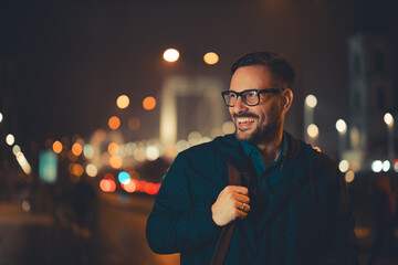 A cheerful adult businessman walking back home during night and admiring the city