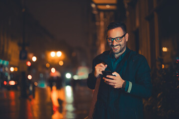 A happy mid adult businessman with glasses scrolling through his phone while going back home from...