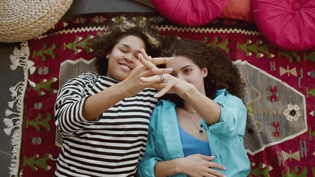 Top-down portrait footage of attractive young women in love relaxing on floor close to each other tenderly touching hands of each other